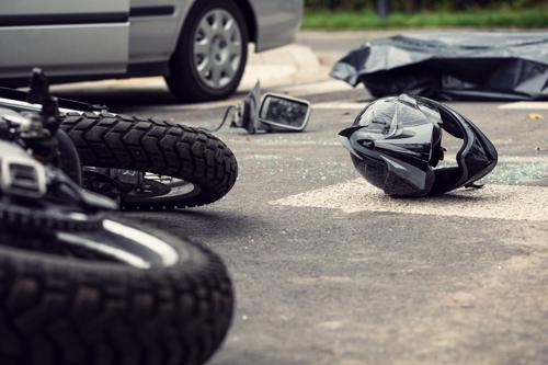 A motorcycle an helmet lying in the road next to pieces from a car after an accident.