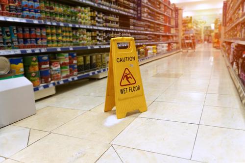 A wet floor in a supermarket with a sign warning patrons of the hazard.
