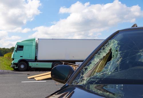 A closeup of an SUV windshield damaged in an accident with a tractor-trailer in the background..